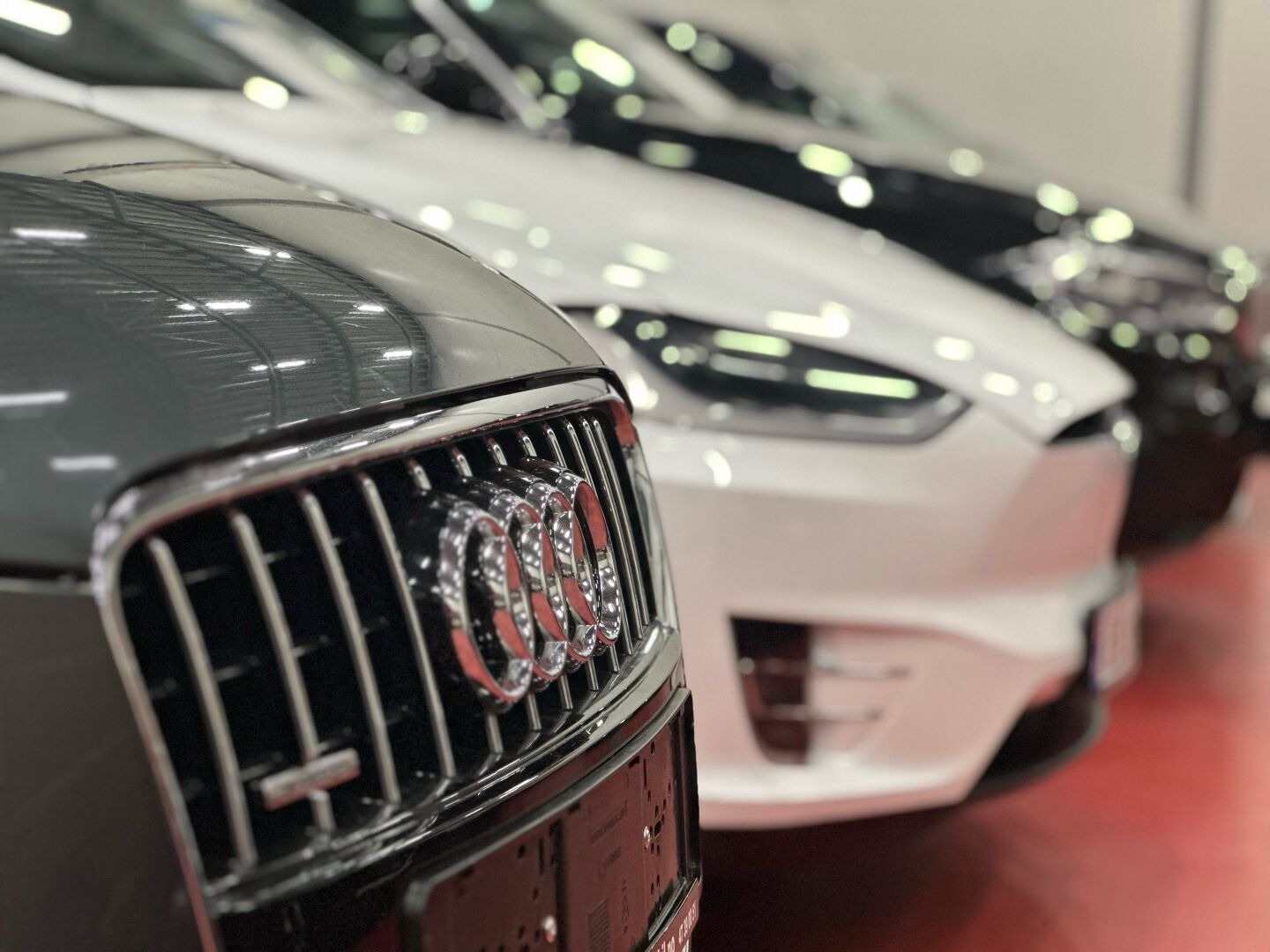 Nærbilde av grillen på en Audi, med flere biler uklart i bakgrunnen.